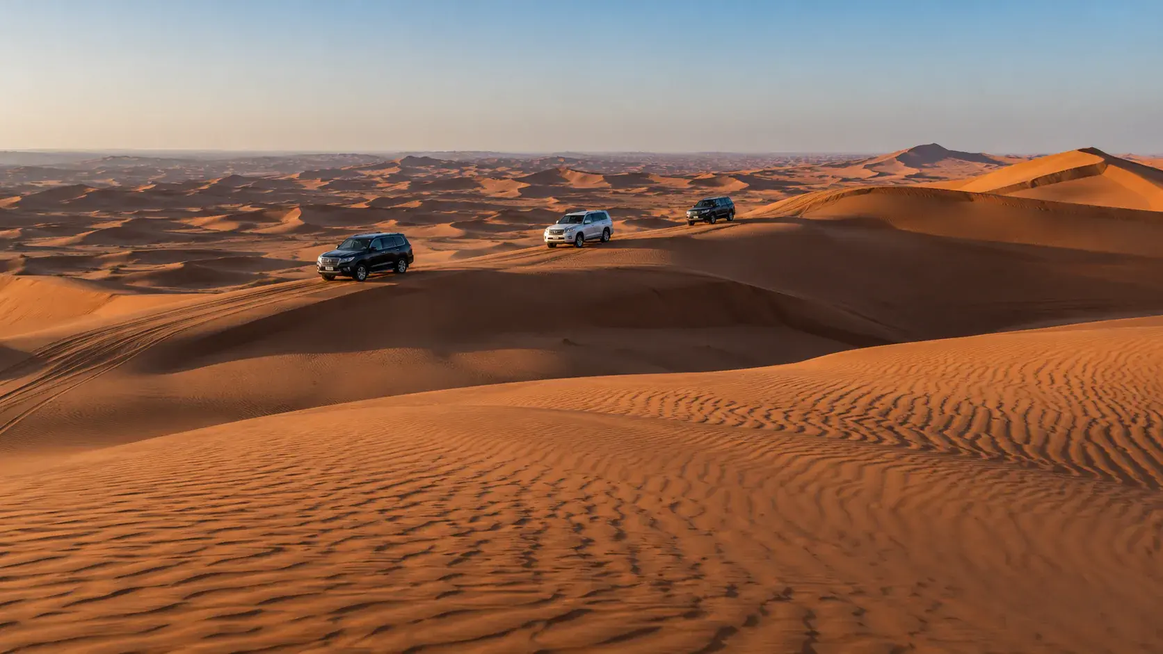 Illustration of three 4x4s crossing rippled orange dunes at dusk