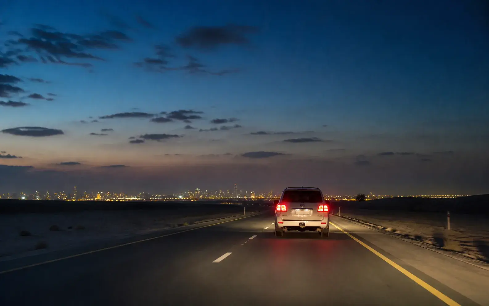Safari vehicle returning toward the illuminated Dubai skyline after a desert evening