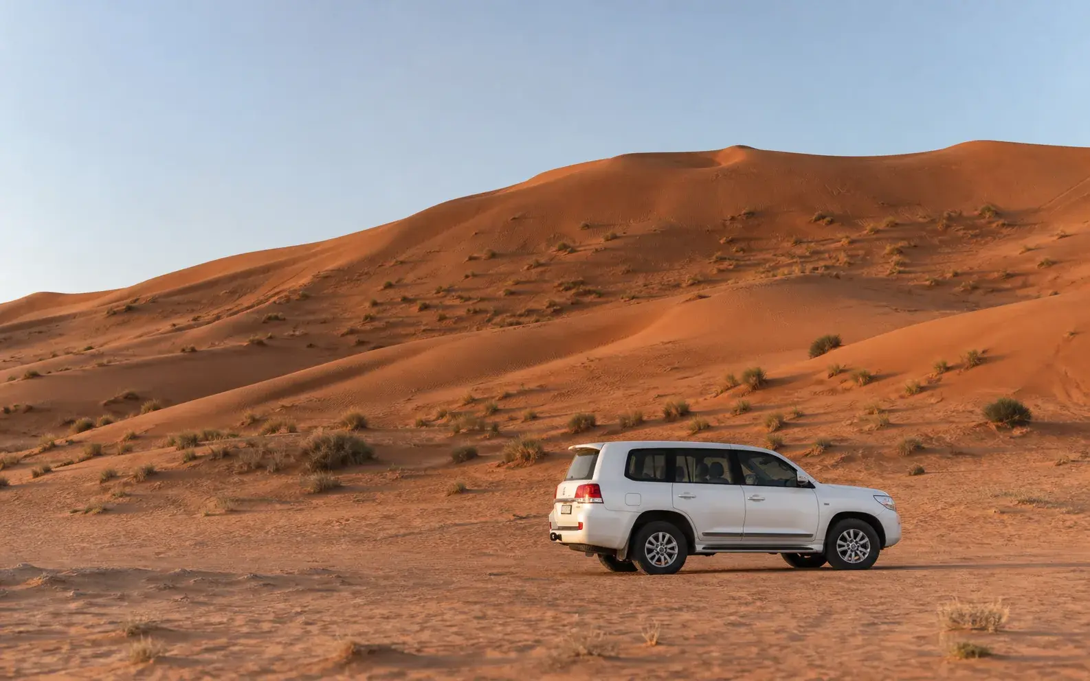 White safari 4x4 arriving below broad red-dune ridges in the Lahbab area