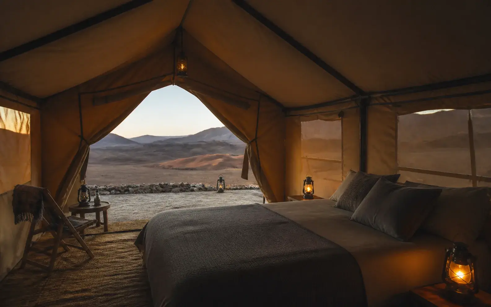 Made-up bed inside a tent, lit by a lantern
