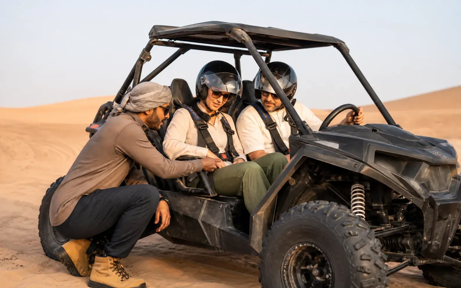 Guide checking a rider's secured helmet beside a parked roll-cage dune buggy