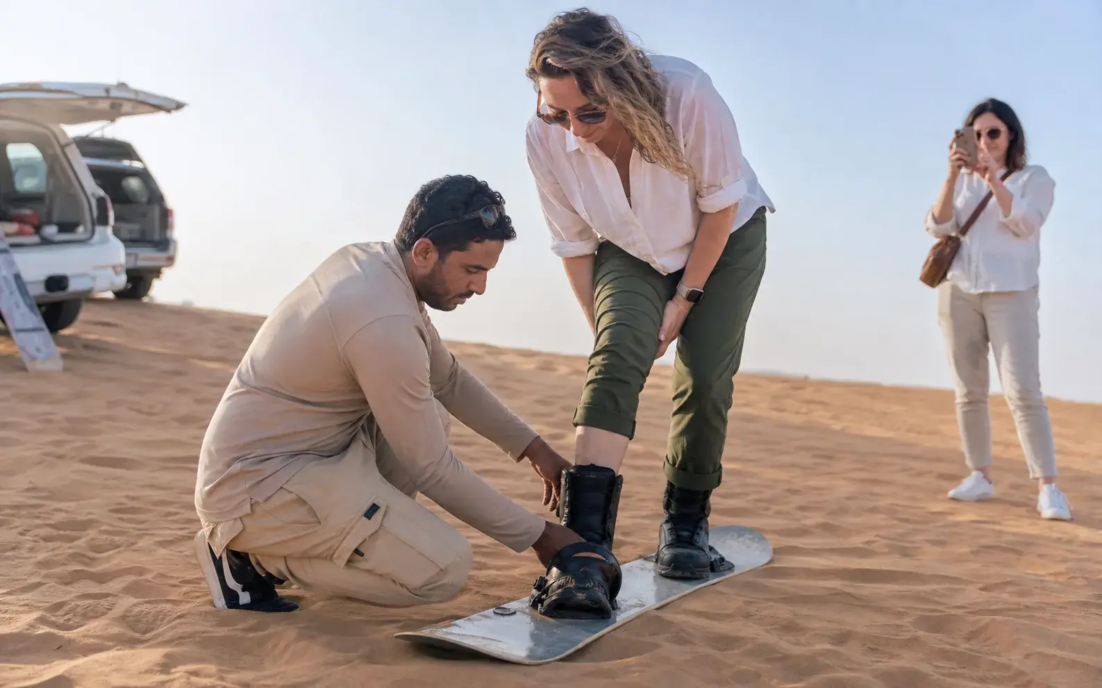 Traveller sandboarding down a clean dune slope in bright morning light