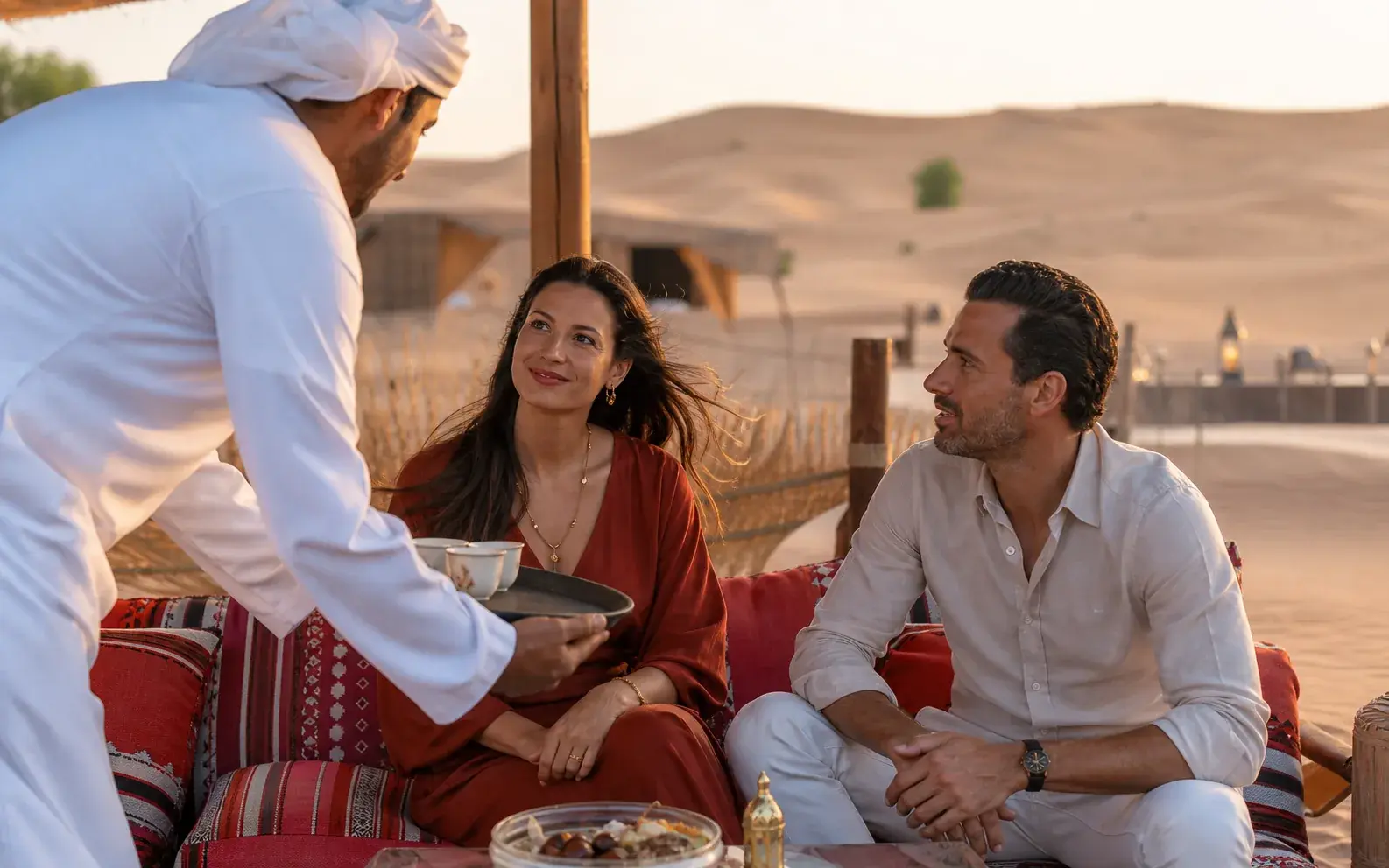 A host serving guests at a softly lit desert camp table