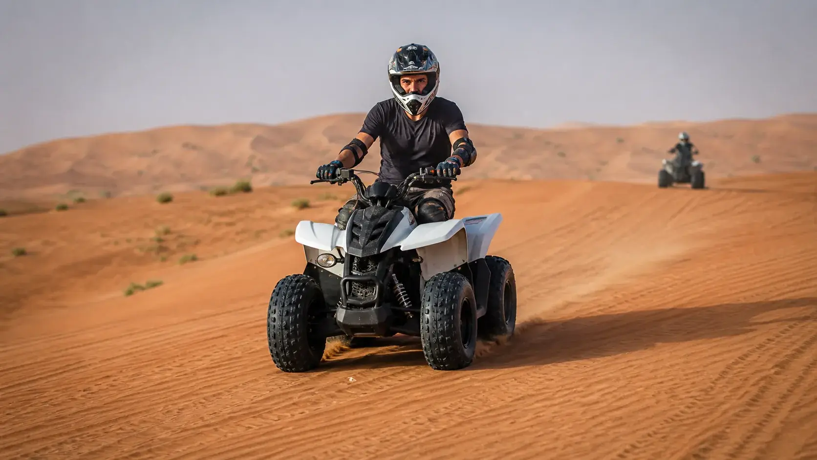 Helmeted quad-bike rider following a guided route across Dubai red dunes