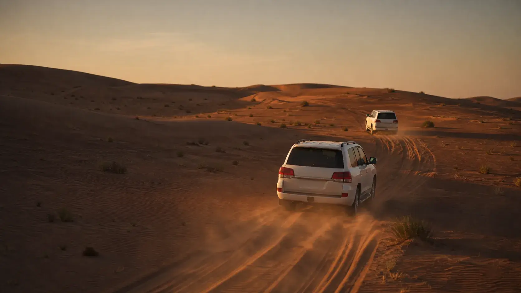 Two unbranded safari vehicles crossing Dubai red dunes at sunset