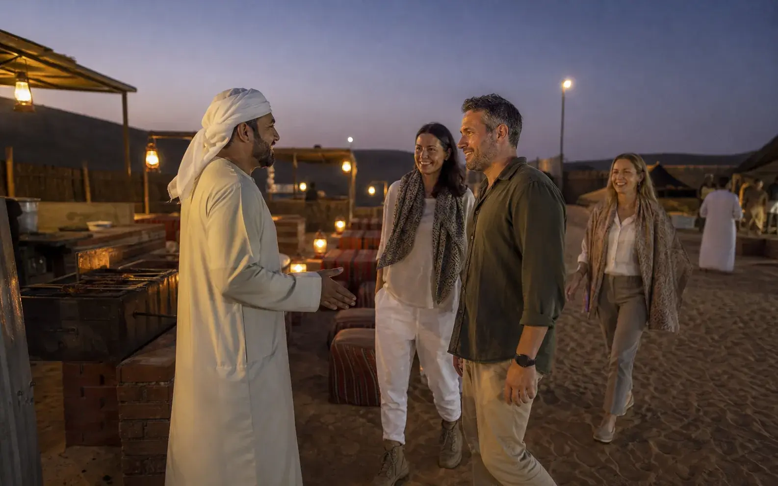 Guests talking at an evening desert camp as the lanterns come on